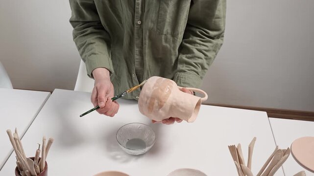 4K Video artist uses a wide studio paintbrush to apply thick glaze to a bisque ceramic bowl for an artistic finish. Artisan Glazing Ceramic Bowl with a Brush