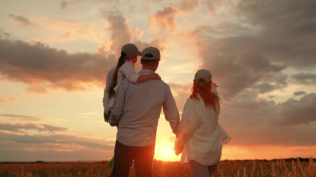 Kid daughter sits in father arms walk hand in hand with mother wheat field sunset. Happy farming family with child strolls wheat field. Farmers, dad mom child girl outdoors together, enjoying, sun sky