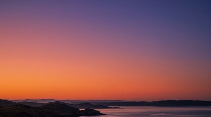 Naklejka premium Vibrant sunset sky over calm water and distant hills with purple and orange hues