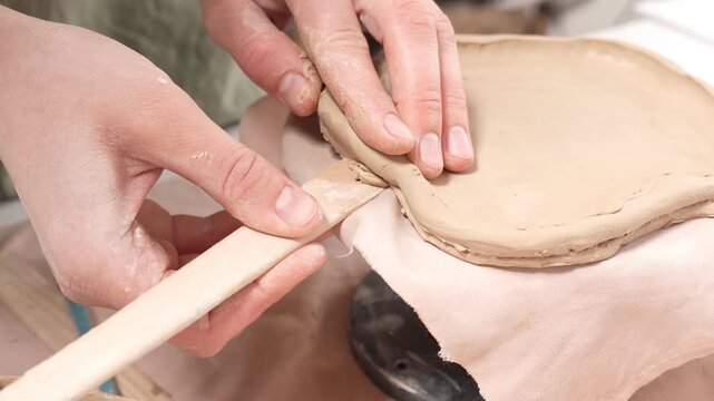 4k video showing an artisan shaping a clay vessel on a banding wheel. The artist slowly rotates the handmade dish while using a wooden tool to refine the rim and achieve a precise, custom finish