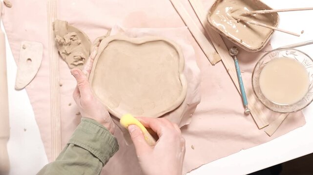 4k video of an artisan refining clay edges with a damp sponge. close-up footage captures the gentle manual technique of wiping the border of an earthenware slab to smooth out surface imperfections