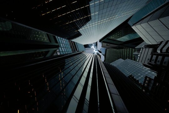 Dramatic low angle worm eye view looking up at modern glass skyscrapers converging toward dark moody sky in financial district