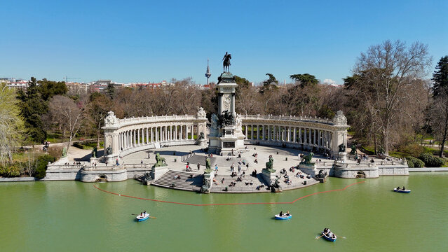 Closer aerial perspective of the Monument to Alfonso XII in El Retiro Park with visitors on the steps, rowing boats on the lake and elegant semicircular colonnade in Madrid, Spain