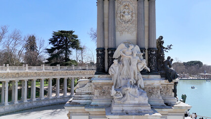 Naklejka premium Close-up drone photograph capturing elegant marble sculptures, classical columns and the lakeside monument of Alfonso XII in El Retiro Park, Madrid, Spain, on a bright sunny day