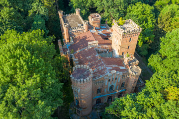 Fototapeta premium Abandoned Neo-Gothic Castle Top-Down Aerial View — Ruined Tudor Manor with Battlements and Round Towers Hidden in Dense Forest | Historic Estate from Above