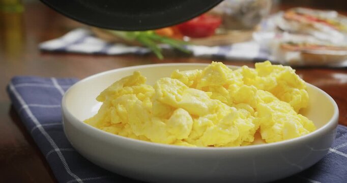 Close up of chef transferring fluffy homemade scrambled eggs from a frying pan onto a white serving plate. Fresh creamy eggs are carefully plated for a delicious homemade breakfast in a cozy kitchen.