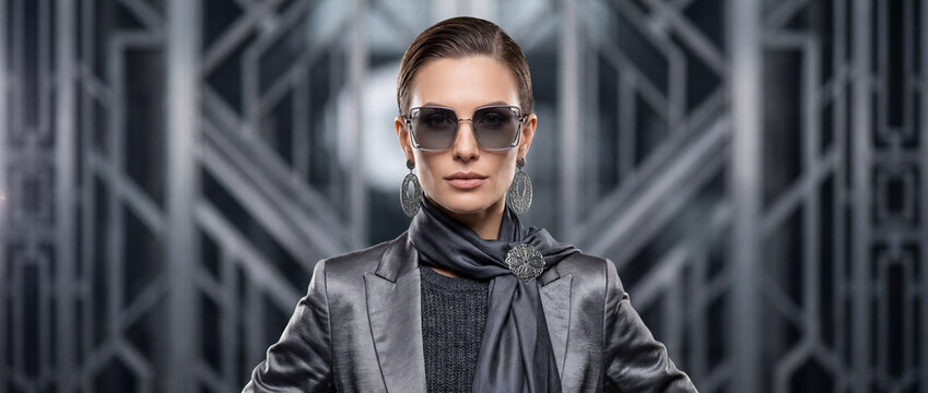 Sophisticated woman in luxury gray suit and sunglasses poses confidently