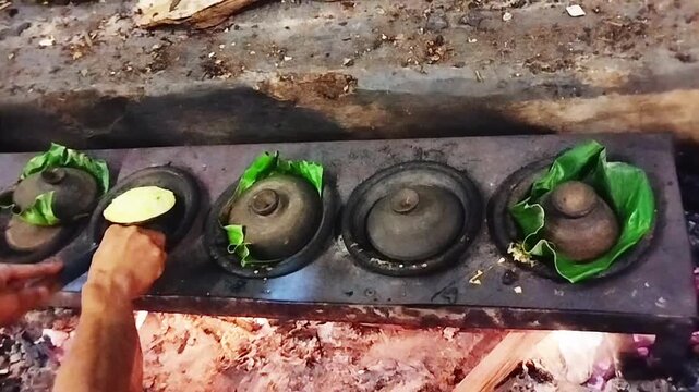 Traditional Sundanese surabi rice and coconut pancakes cooking in clay pots over a wood fire with banana leaves, Indonesian traditional food preparation, cultural cooking footage.