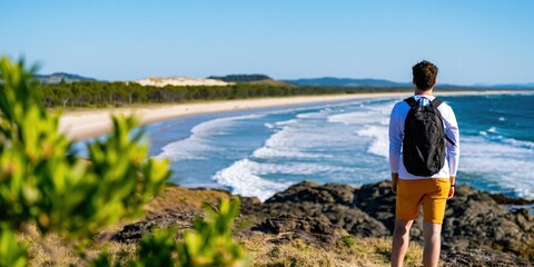 Naklejka premium Man hiker with backpack standing on a rocky cliff overlooking the ocean beach view