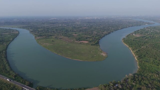 Spectacular high altitude aerial view of a huge Tuxpan River in Mexico forming a perfect meander, surrounded by a lush green forest and fields with a distant city visible on the hazy horizon
