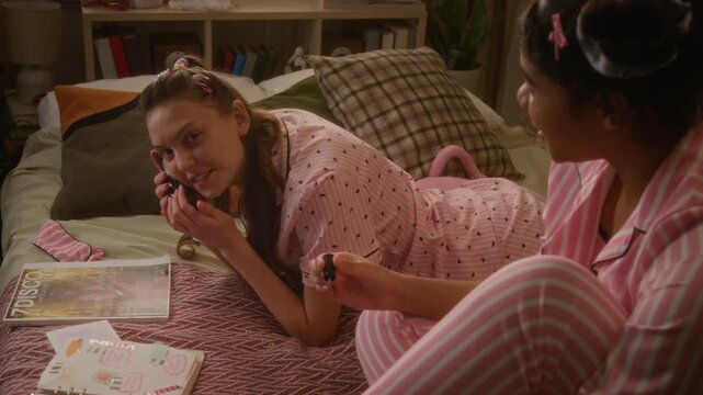Caucasian teenager talking on retro phone and laughing during sleepover with African American friend, sharing fun gossip. Clip is ideal for youth lifestyle marketing and telecommunication campaigns