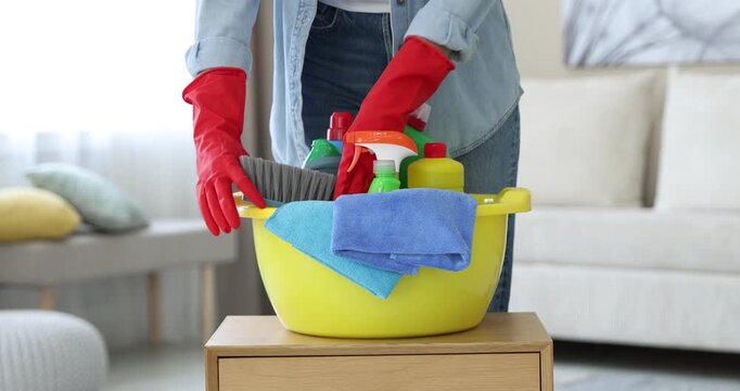Woman putting plastic basin with cleaning products and supplies on wooden table in room, closeup