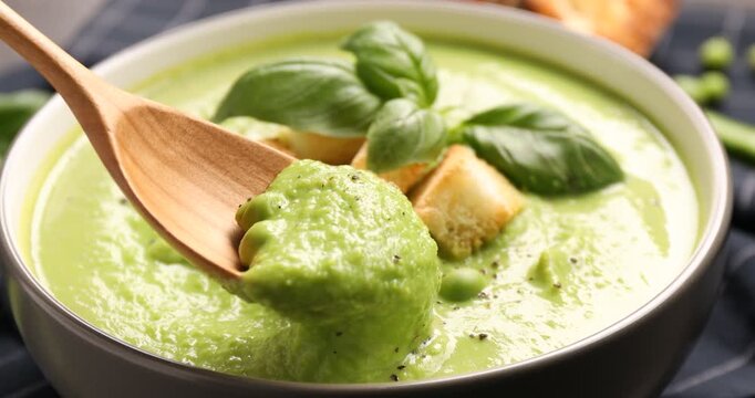 Eating delicious pea cream soup with croutons and basil at table, closeup