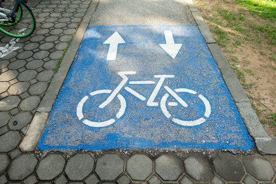 Close-up of blue bike path with direction arrows and bicycle icon on city street.