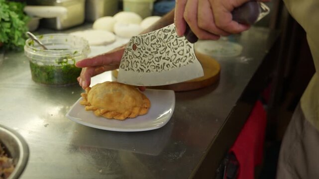 Chef cutting a freshly fried empanada and adding garnish