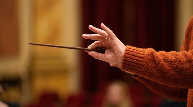 Close up of a female conductor hand holding a baton during a classical music rehearsal in a concert hall