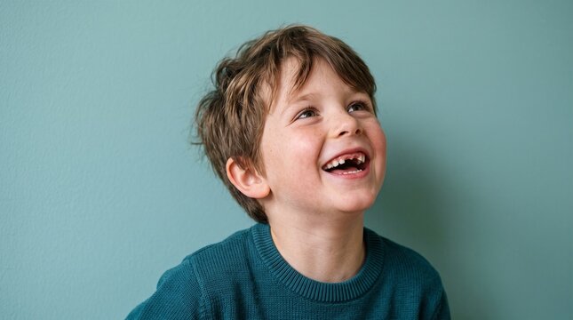 Joyful young boy with missing front teeth laughing heartily against a teal background