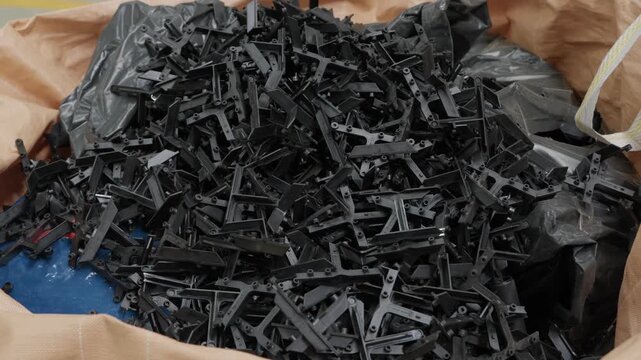Pile of black injection molded plastic parts collected in bulk bag for recycling