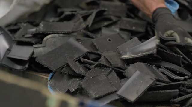Shredded black plastic scrap pushed and sorted by hand before grinding at recycling plant