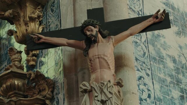 Carved crucifix of Jesus Christ on a black cross beside blue azulejo tiles inside a church