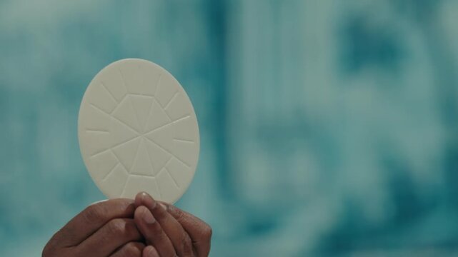 Hands raise a white communion host with embossed cross during the celebration of Catholic mass