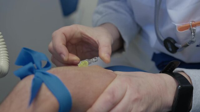 Nurse hands insert a cannula into a patient arm with a blue tourniquet tied above the elbow