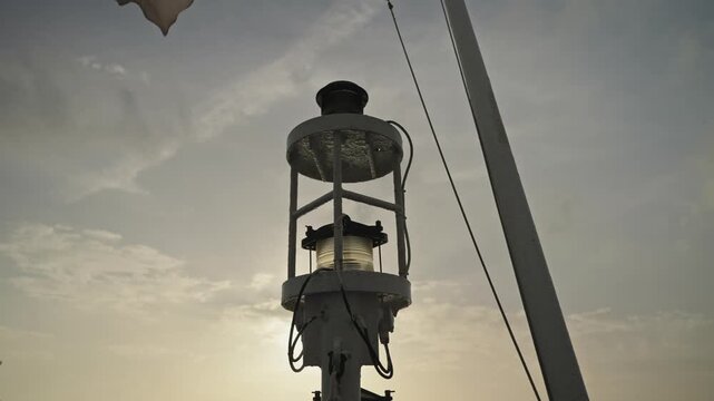 Boat mast navigation lamp with cables and rigging against golden sunset sky