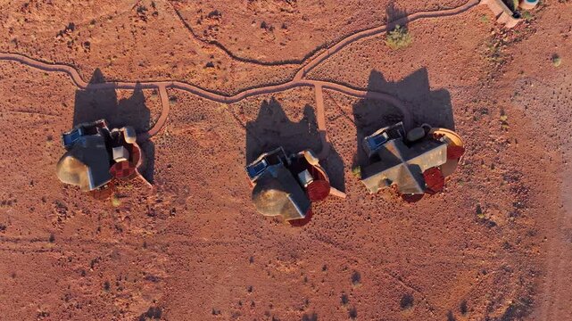 Drone view of curved rows of lodge chalets on the red sand plains of the Namib desert. The remote eco retreat blends into the red desert landscape beneath wide skies and distant mountains.
