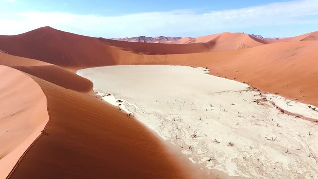 Aerial drone shot of deadvlei in the Sossusvlei dune sea. The towering red dunes glow against the pale cracked clay pans of this ancient desert wilderness. High view of famous dead trees from above.