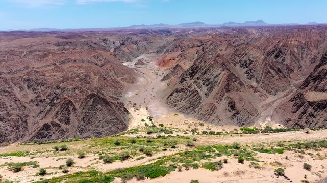 Aerial view of a green ephemeral watercourse crossing an arid Namibian plain, scattered desert vegetation marking the hidden line of water below.
