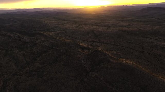 Drone footage of golden sunrise light raking low across rugged desert terrain in central Namibia, long shadows revealing the textured land.