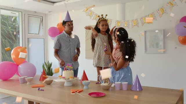 Man leaning forward adjusting cake, family crowning child and blowing horns, confetti for birthday