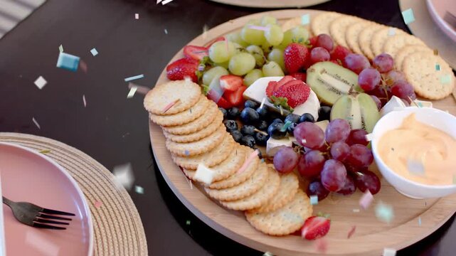Confetti falling above camera tilting showing board with crackers, fruit, cheese for event