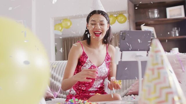 Woman using blower and tossing confetti while glancing at tablet showing animation, hosting stream