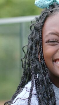 Vertical video: Smiling child laughing as camera framing right side at park, braids bow sweater