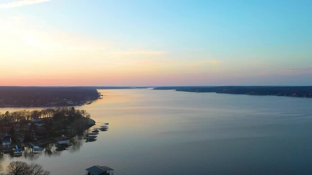 Scenic Branson, Missouri lake aerial with calm water, forested Ozark shoreline, lakeside homes, covered docks, and colorful evening sky for travel, tourism, or vacation footage.