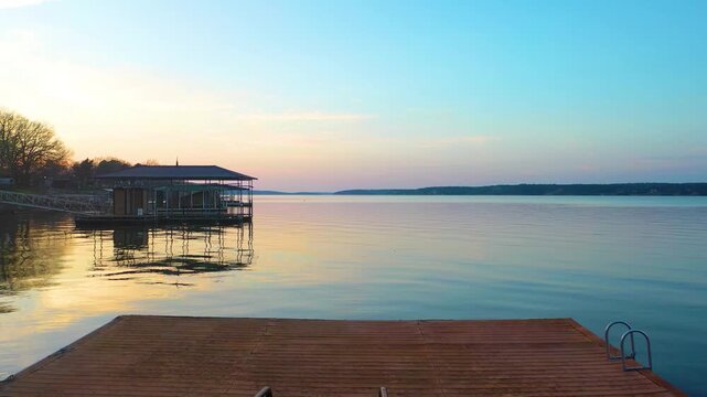 Peaceful Branson, Missouri drone view with lakefront homes, covered boat docks, forested Ozark coves, calm evening water, and warm sunset glow across a scenic vacation lake landscape.