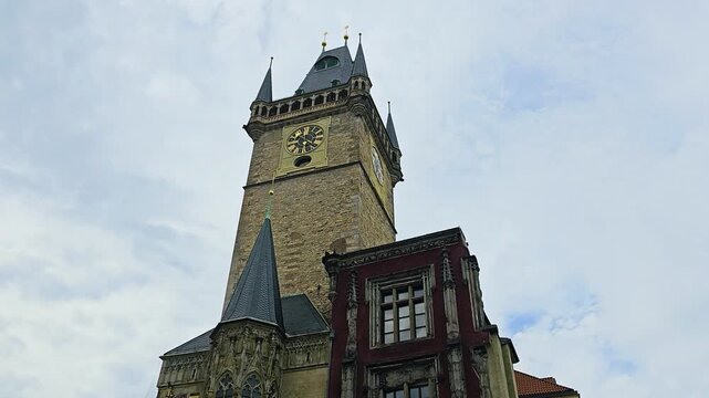 Upward view of Prague&rsquo;s medieval clock tower and Gothic architecture, with ornate windows, stone carvings, golden clock face, and cloudy sky in Old Town Square, Czech Republic.