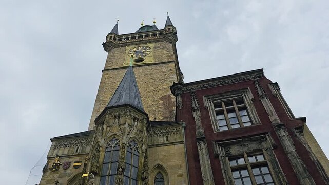 Low angle view of the Prague Astronomical Clock tower in Old Town Square, showing Gothic architecture, ornate stone details, historic clock face, and cloudy sky over Prague city.
