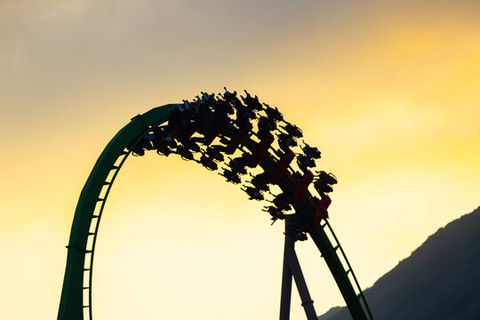 People riding rollercoaster at sunset in amusement park