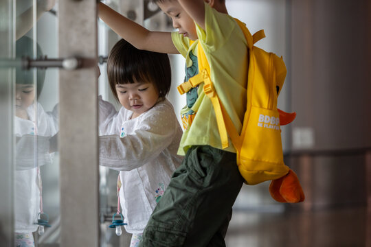 Two asian children playing near glass railing