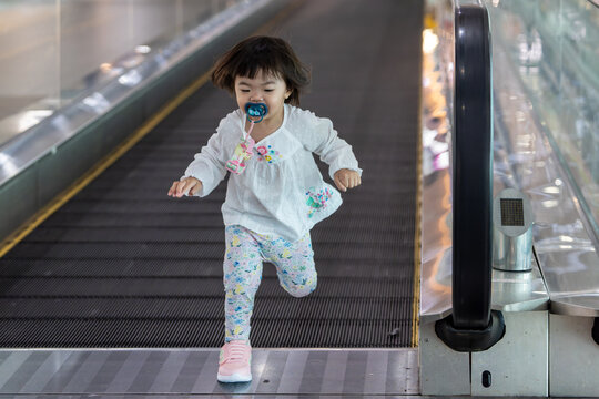 Little girl running on moving walkway in airport terminal