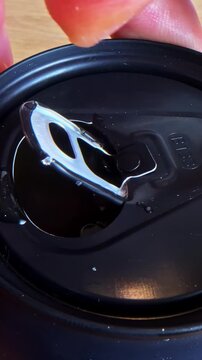 A close-up view of a beverage can being opened, capturing the metallic click and droplets.