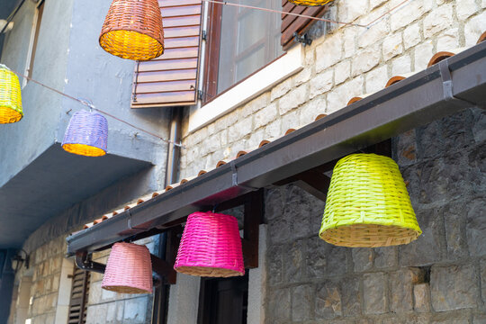 Close-up of colorful woven hanging lamp shade basket in yellow, orange and pink against a building facade, decorative craft.