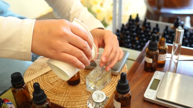 Close-up of hands filling a perfume bottle during handmade fragrance production with essential oils in an artisan workshop. DIY cosmetics, precision blending, small business, luxury scent, and creativ