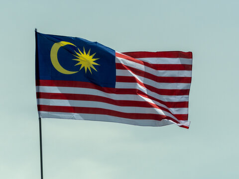 Malaysian national flag Jalur Gemilang waving against a light blue sky, symbolizing national pride.