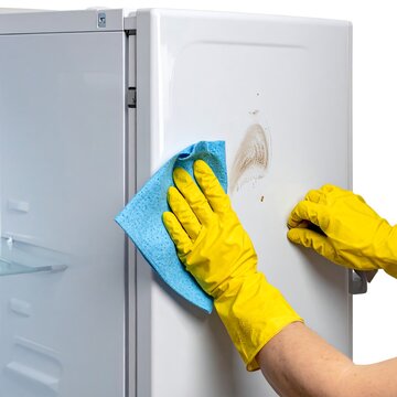 Person wearing yellow gloves cleaning a white refrigerator with a blue cloth