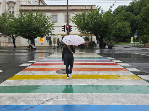 Woman with crossing rainbow colored crosswalk in Salzburg, Austria on rainy overcast summer afternoon.