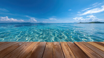 Fototapeta premium A serene tropical beach with clear turquoise water and a wooden deck in the foreground, under a vast blue sky.