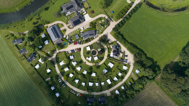 Aerial view of a circular campsite layout with numerous caravans, small buildings, and manicured green lawns, situated near the winding Berkel river in Almen, Gelderland, Netherlands.